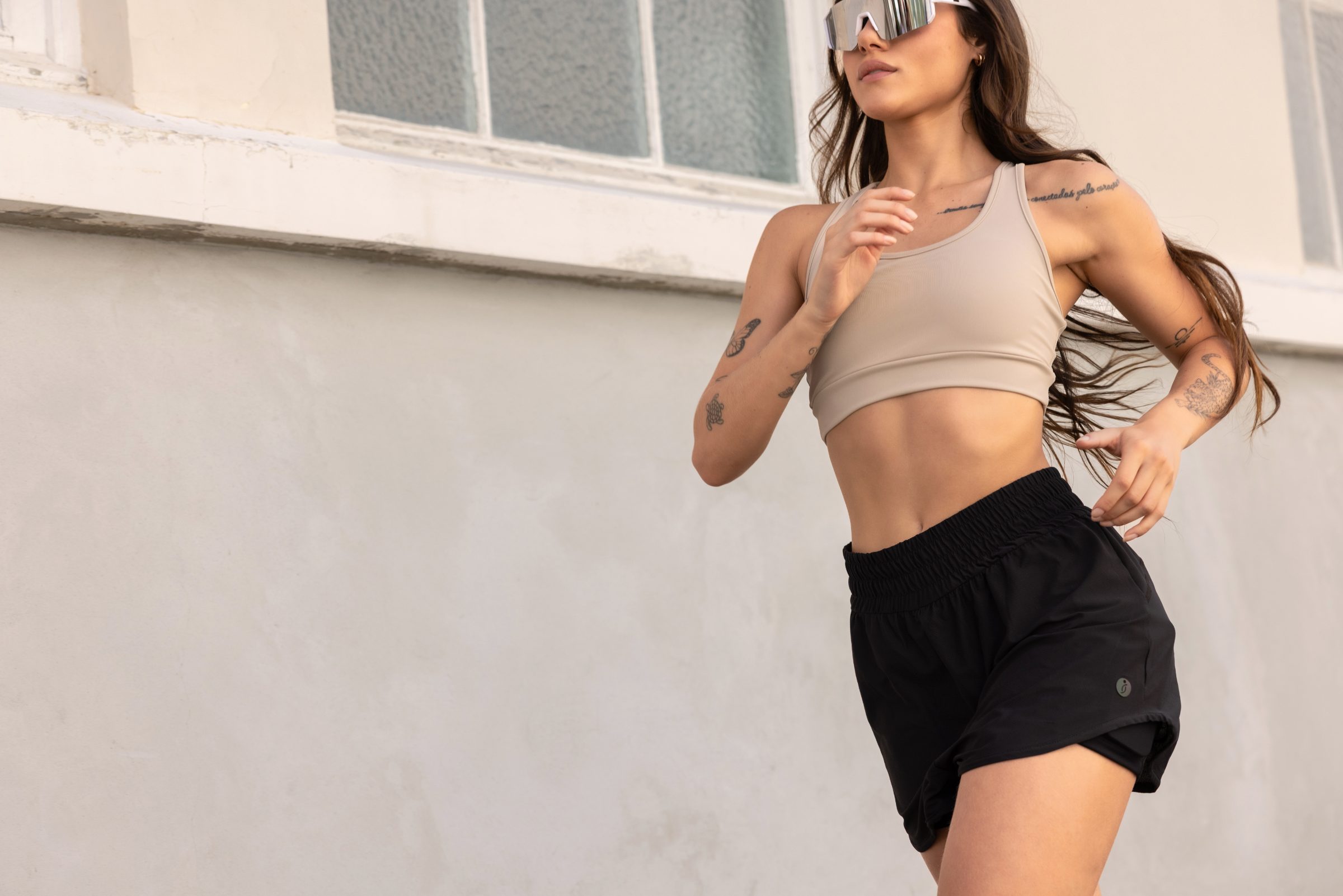 Mulher correndo na rua com top nude e shorts preto Físico, luz natural