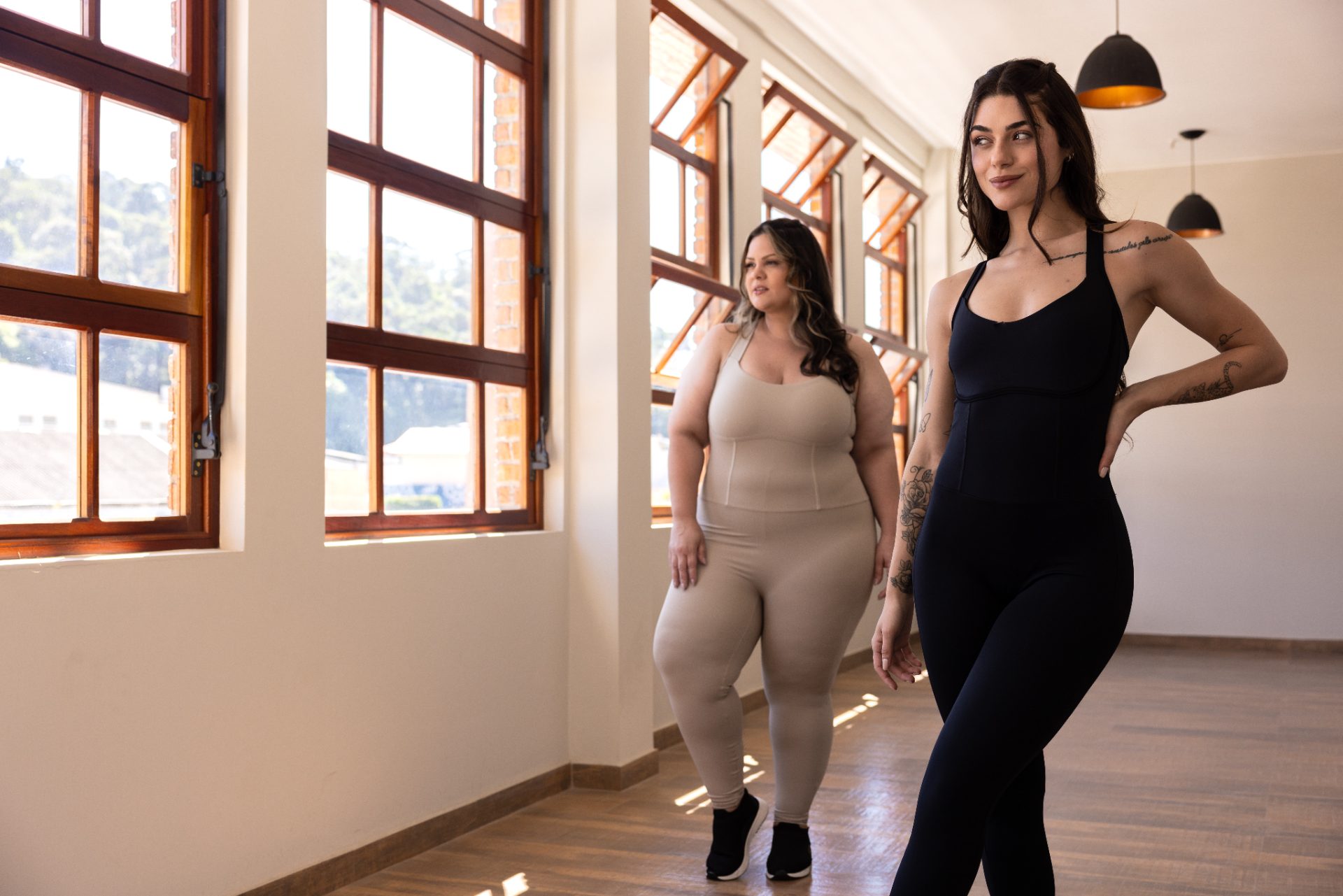 Duas mulheres de biotipos diferentes caminhando juntas depois do treino, em luz natural